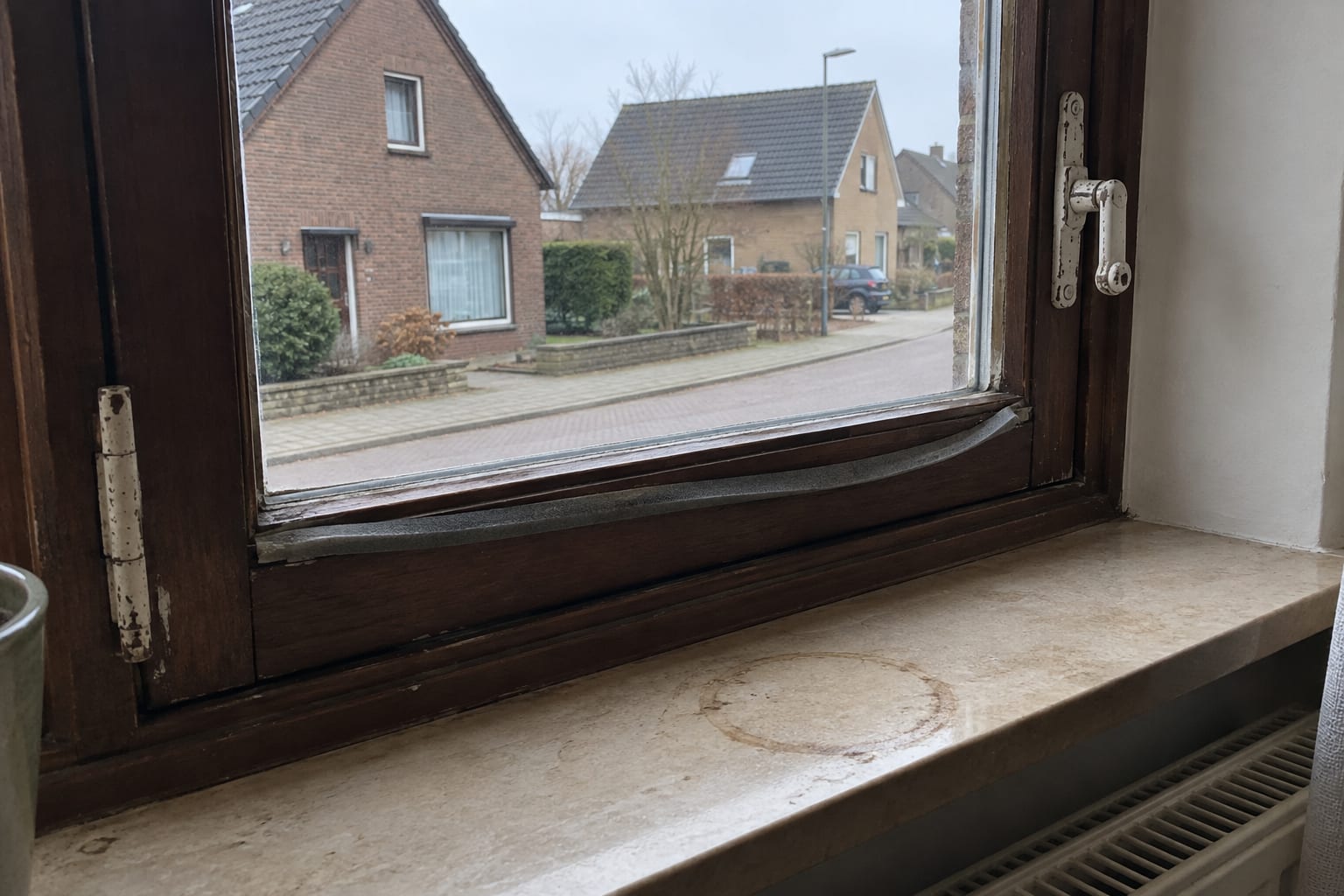 Oud houten raam met enkel glas en een losgeraakte tochtstrip, van binnen gezien