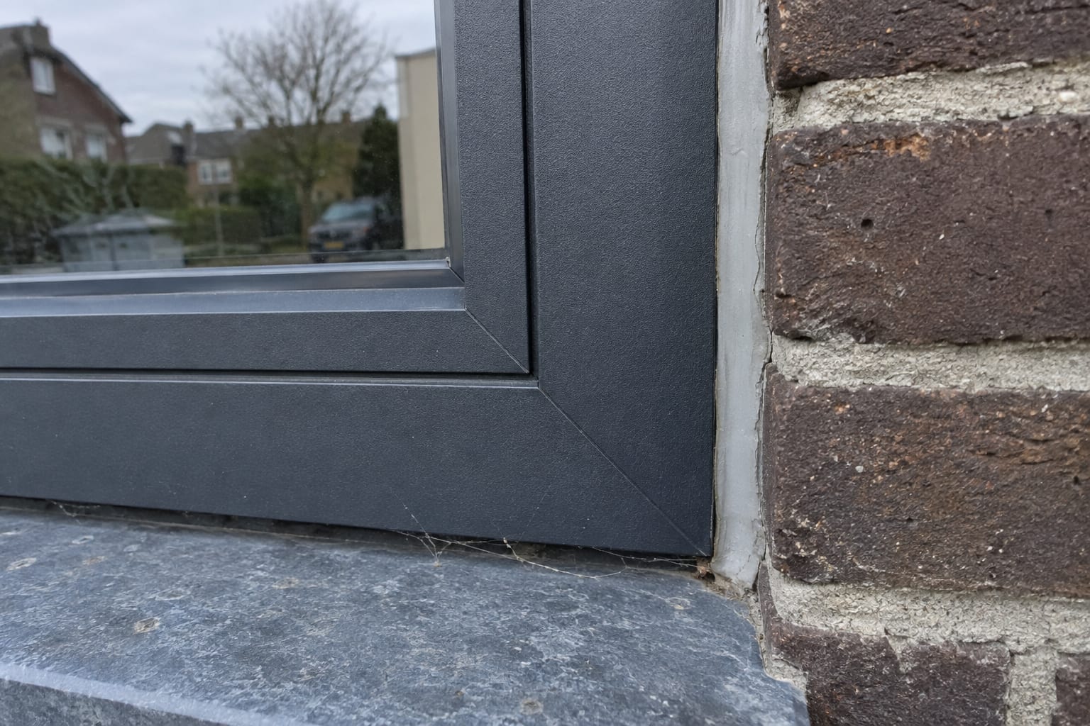 Onderhoek van een antraciet aluminium kozijn in donkere baksteen